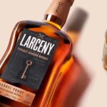 Botella de LARCENY Bourbon Whiskey con un vaso lleno de whisky al lado.