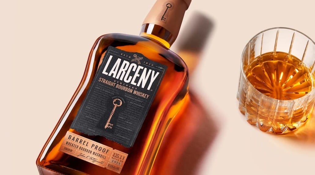 Botella de LARCENY Bourbon Whiskey con un vaso lleno de whisky al lado.