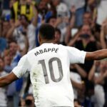 Jugador celebrando un gol mientras los aficionados vitorean en el estadio.