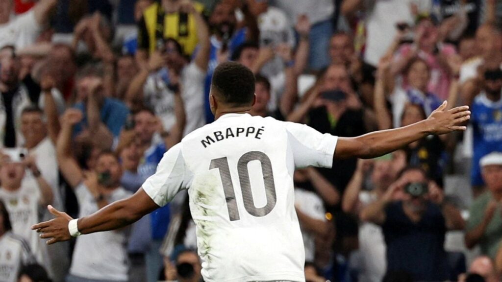 Jugador celebrando un gol mientras los aficionados vitorean en el estadio.